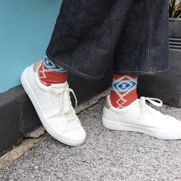 man wearing aztec patterned socks against a blue wall wearing white trainers